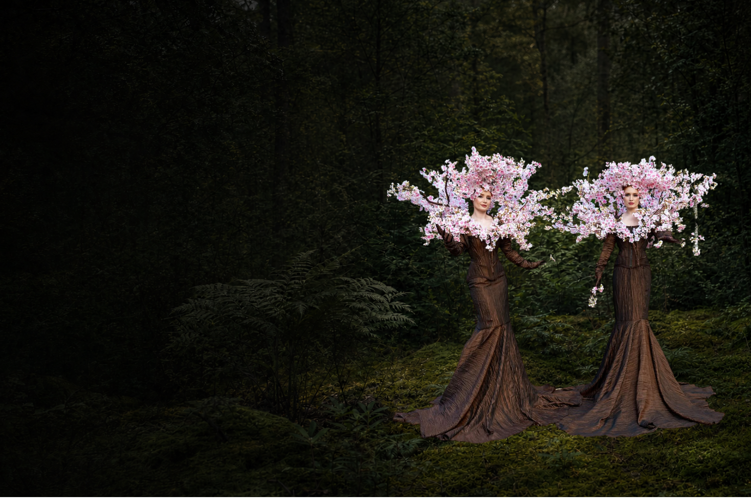 Two botanical performance artists in sculptural cherry-blossom headpieces within a garden