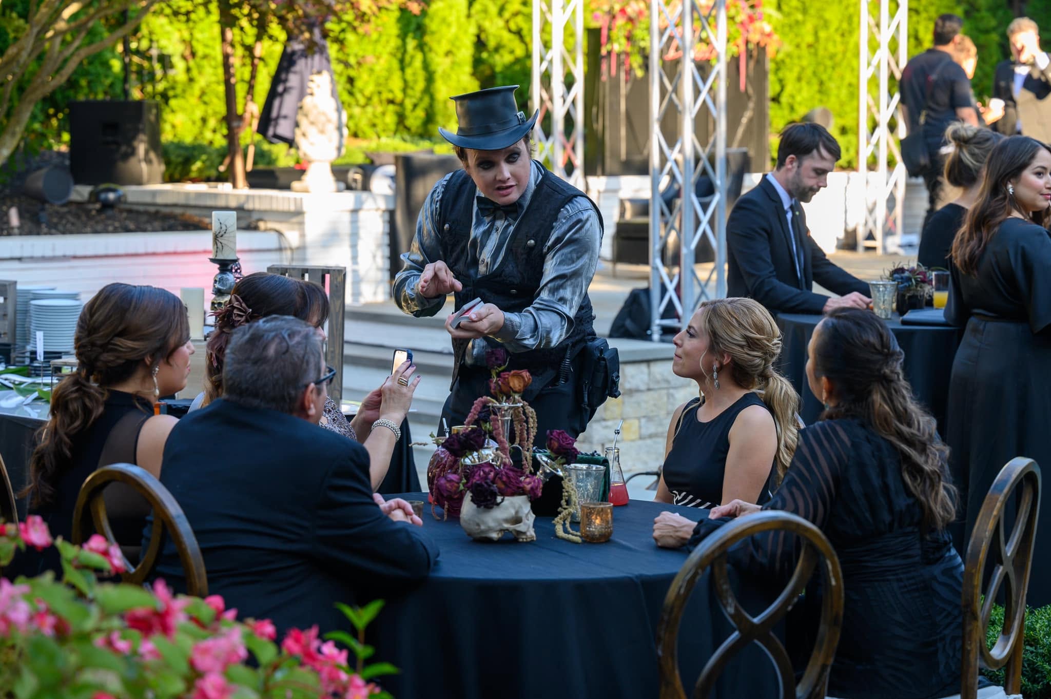 A top-hat performer shares a close-up card performance with seated guests