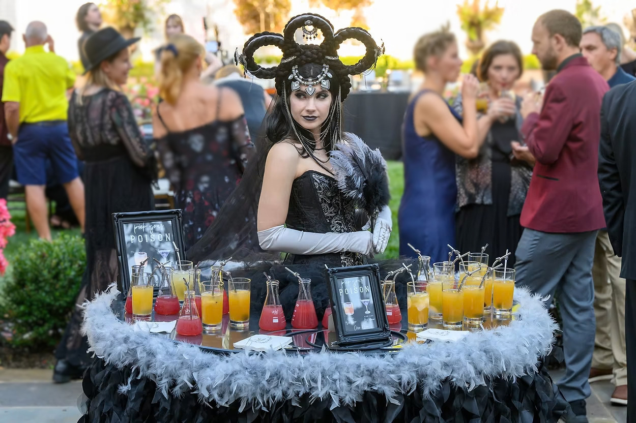 Living Table performer with a braided headpiece, feathered table and custom cocktail display among event guests