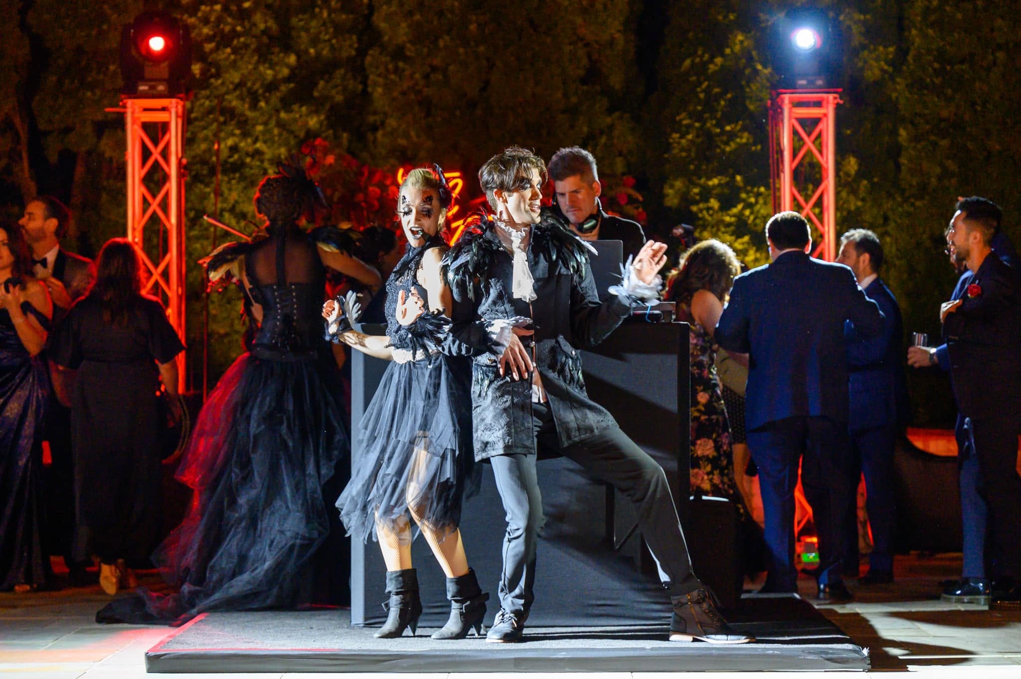 Two costumed dancers performing beside a DJ and event guests at night