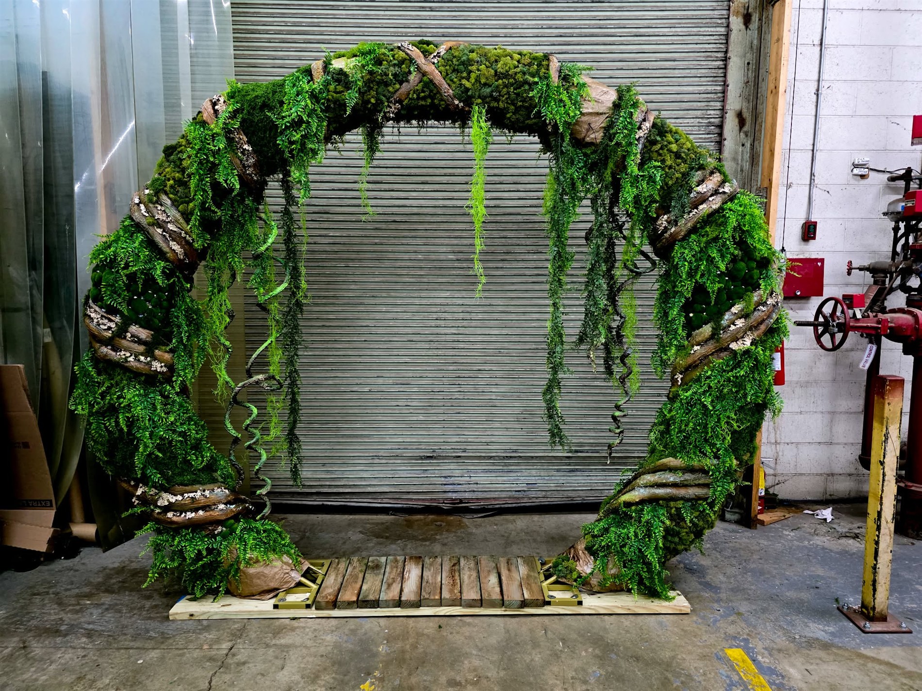 A large scenic arch covered in moss, ferns, and sculpted branches in the workshop