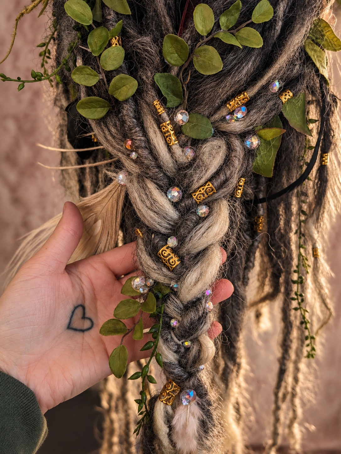 A hand holding a detailed braid embellished with leaves, crystals, and gold beads