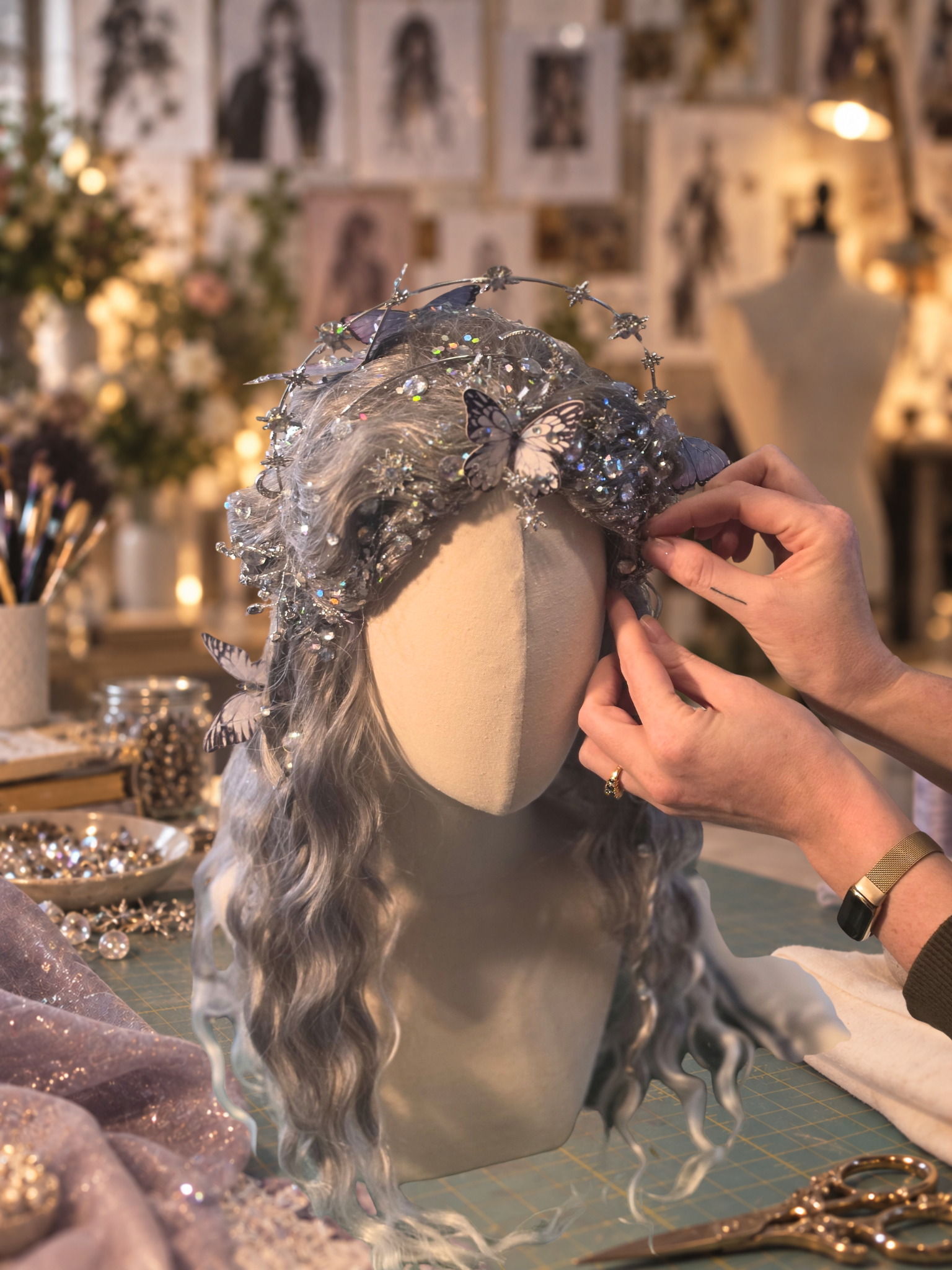 Hands securing butterfly and celestial details to a silver character wig